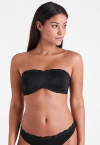 Zwart strapless bandeau bh van gladde stof met een gebogen bovenrand. Een bijpassend zwart kanten ondergoed is ook zichtbaar.