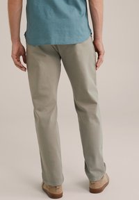 Pantalones rectos de un gris claro, confeccionados en una tela suave, con una textura sutil. Combinados con zapatos beiges, vistos desde atrás.
