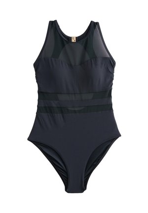 Jeune femme portant un maillot de bain noir sans manches posant en plein air avec un ciel bleu clair en arrière-plan.