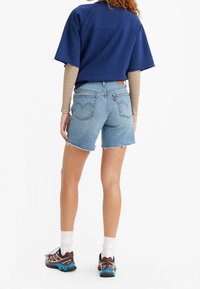 Džínové šortky s třepeným lemem, světle modré barvy, a s označením vzadu; kombinované s námořnickou oversized halenkou a sportovními botami.