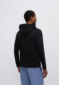 Must pika varrukaga kapuutsiga dressipluus lõdva istuvusega ja esiküljel kängurutaskuga, kombineeritud helesiniste vabaaja pükstega. Sile kangapind.