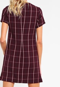 Vestido de manga corta en burdeos con un patrón de cuadros en rosa y azul. Presenta un corte recto y un ajuste holgado. Textura de tela suave.