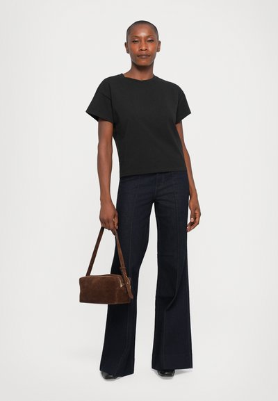 Black cotton t-shirt with short sleeves, paired with dark blue flared jeans. Brown suede handbag with a shoulder strap and a zip closure.