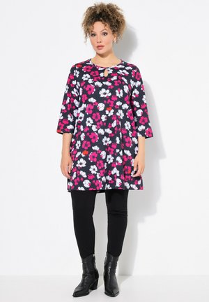 Robe tunique florale en bleu marine, ornée de fleurs roses et blanches, avec un décolleté en forme de goutte d'eau, des manches trois-quarts, associée à des leggings noirs et des bottines.