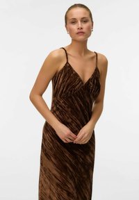 Lang, brun, velourkjole med en tætsiddende silhuet, v-halsudskæring og tynde skulderstropper, der har et struktureret, bølget mønster.