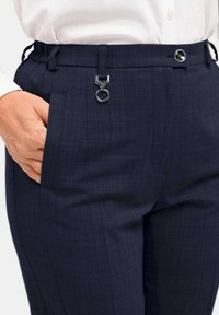 Marineblaue, maßgeschneiderte Hosen aus strukturiertem Stoff, mit elastischem Bund, Seitentaschen und einem metallischen Hardware-Detail für den Verschluss.