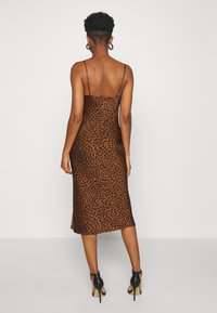 Vestido midi de estampado de leopardo marrón con tirantes finos, silueta ajustada y textura suave, combinado con zapatos de tacón alto negros.