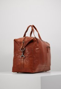 Sac en cuir marron avec deux poignées, une poche zippée à l'avant et un clip métallique. Caractéristiques d'une texture lisse et d'une forme rectangulaire.