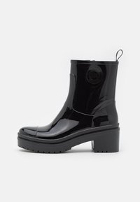 Bottines en cuir verni noir avec un talon épais, un bout rond, une semelle en caoutchouc et un détail de logo embossé sur le côté extérieur.