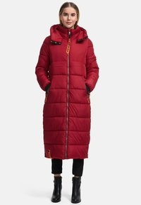 Rode lange pufferjas met een capuchon, ritssluiting, zijzakken en een textuur quilting. Heeft zwarte accenten en een oranje label.