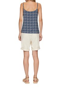 Marineblauw patroon top met dunne bandjes, gecombineerd met crèmekleurige opgerolde shorts en neutrale sandalen. Casual zomerset.