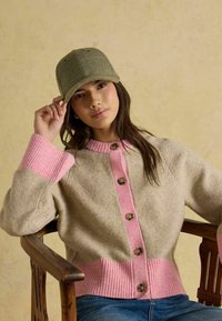 Cardigan bej din lână cu manșete și tiv roz cu dungi, cu nasturi rotunzi pe partea din față. Șapcă verde măsliniu cu textură netedă.