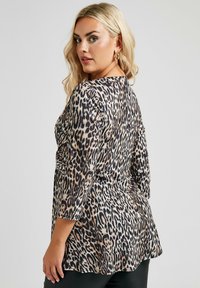 Tunika con stampa leopardata e maniche 3/4, caratterizzata da una vestibilità ampia e un tessuto morbido. La palette di colori include tonalità di nero, marrone e beige.
