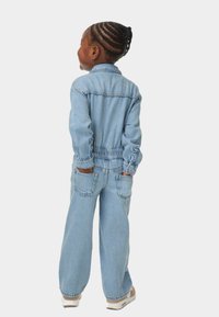 Leren jumpsuit in lichtblauw met lange mouwen, elastische tailleband en grote achterzakken. Heeft een ontspannen pasvorm en opgerolde mouwen.