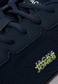 Baskets bleu foncé en tissu texturé avec lacets, avec le logo "Jack & Jones" en blanc et vert sur le côté.