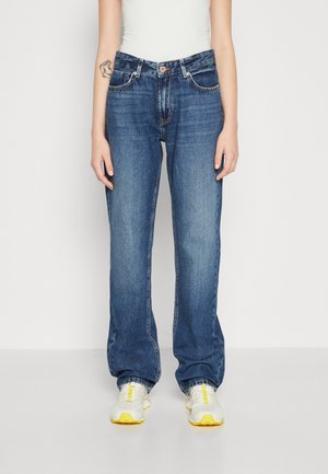 Donkerblauwe denim jeans met een rechte pijp, vijfzakkenontwerp, oranje stiksels en een klassieke knoopsluiting, gecombineerd met grijze sneakers.