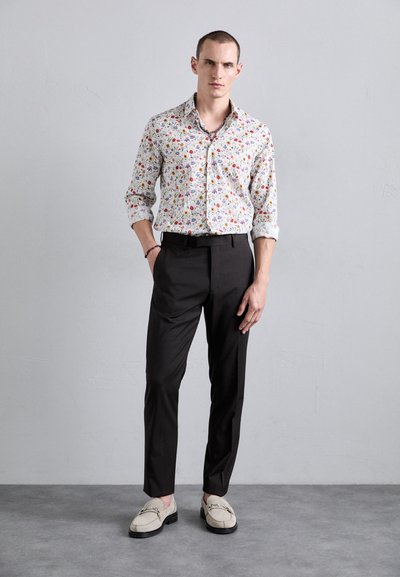 Floral print button-up shirt, white base with multicolored flowers, paired with black trousers and beige loafers, standing pose.