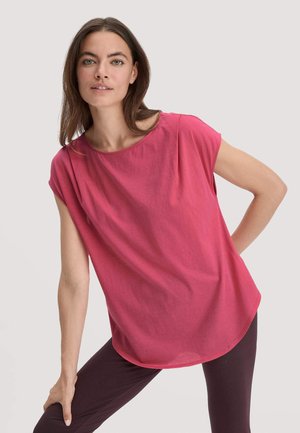 Top rosa a maniche corte in tessuto morbido con scollatura tonda e vestibilità comoda. Orlo curvo e maniche arrotolate. Abbinato a leggins scuri.