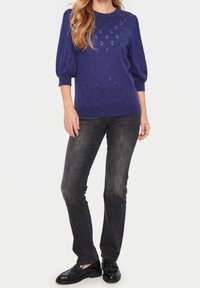 Lila stickad tröja med korta puffärmar som har ett texturerat mönster. Kombinerad med mörkgrå jeans och svarta skor.