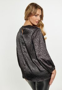 Schwarze Bluse mit Leopardenmuster, glatter Textur, langen Ärmeln und einem Rückenschlitz. Lockere Passform mit dezentem Glanz.