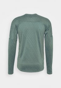 Long-sleeve shirt in textured dark green fabric, featuring a subtle striped pattern and rounded neckline. Includes side pocket detail.