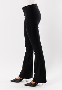 Pantaloni neri a zampa d'elefante con una texture liscia, vita alta, cuciture laterali e una silhouette aderente, abbinati a tacchi a punta.