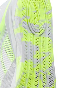 Close-up do solado com padrão em verde neon e cinza de um ténis branco, com superfície texturizada e marcas da marca.