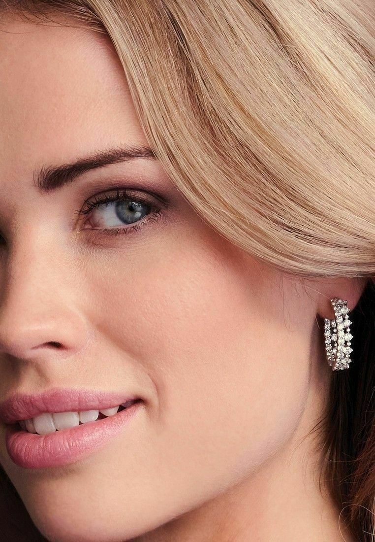 Silverfärgade ringörhängen med flera glittrande rhinstenar; slät textur och kurvig design som visar en modern och elegant look.