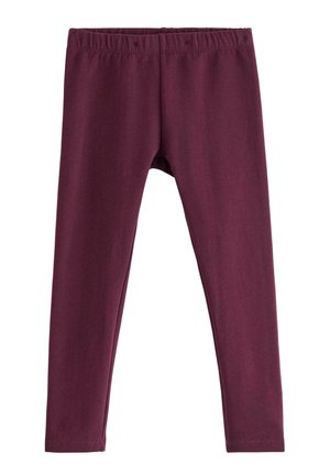 Barn med krøllet hår iført vinrød sweatshirt og leggings, stribede ærmer og sokker, poserer med det ene ben løftet mod hvid baggrund.