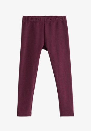 Barn med krøllet hår iført vinrød sweatshirt og leggings, stribede ærmer og sokker, poserer med det ene ben løftet mod hvid baggrund.