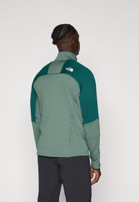 Fleece jacket in two shades of green, featuring a high collar and textured fabric. Logo printed on the upper back. Tailored fit, long sleeves.
