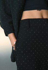 Black, textured fabric pant with scattered silver sequins; fitted design includes side pockets and a flat waistband.