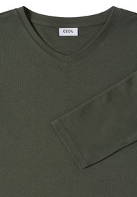 Haut à manches longues en vert olive avec col en V, fabriqué en tissu doux, comportant une étiquette "CECIL" et des coutures soignées le long de l'encolure et des manches.