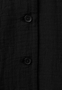 Gros plan d'un tissu noir texturé avec deux boutons de couture noirs alignés verticalement et des boutonnières sur le côté gauche.