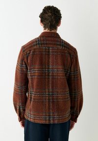 Brown plaid flannel shirt, textured fabric, featuring a collar and long sleeves, with additional blue and red lines in the pattern.