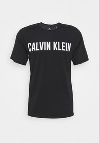 Černé tričko s krátkým rukávem s velkým bílým nápisem "CALVIN KLEIN" na prsní části a kulatým výstřihem.