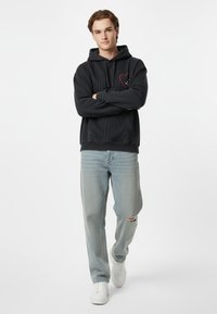 Felpa nera con un design testurizzato, con una grafica di un cuore rosso sul petto. Abbinata a jeans chiari strappati e sneakers bianche.