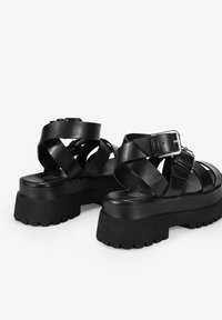 Sandali platform neri in pelle liscia, con cinturini incrociati, una fibbia argentata e una suola in gomma texturizzata per una migliore aderenza.