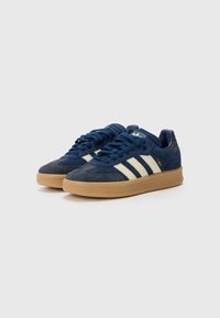 Zapatillas de deporte azul marino con materiales de ante y textil, que presentan rayas blancas, suelas de goma color beige y un diseño texturizado.