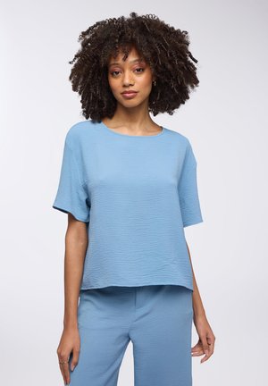 Top azzurro chiaro, texturizzato, con una vestibilità ampia, scollo rotondo e maniche corte, abbinato a pantaloni corti dello stesso materiale e colore.