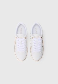 Coppia di sneakers bianche Guess con lacci bianchi, occhielli dorati e logo del marchio dorato sulla linguetta, viste dall'alto su sfondo bianco.
