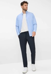Helles blaues Button-Up-Hemd über einem weißen T-Shirt; dunkle Hose mit Kordelzug; weiße Sneaker. Lässige Passform mit minimalen Designelementen.