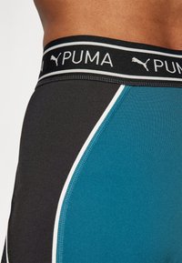 Zbliżenie na osobę noszącą niebieską i czarną bieliznę Puma z markowym elastycznym pasem i białymi detalami.