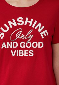Rode katoenen T-shirt met een ronde halslijn en korte mouwen. De tekst op de voorkant bevat "SUNSHINE Only AND GOOD VIBES" in witte en zilveren letters.