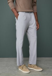 Light gray trousers made of textured fabric, featuring a tailored fit, vertical crease, and side pockets, paired with beige sneakers.