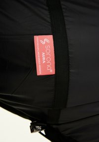 Zwarte lichte jas met een zachte textuur en een felroze label met de tekst "sorona AURA" voor ademend vermogen en warmte.