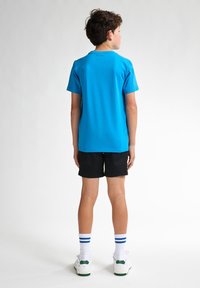 Camiseta de algodón azul de manga corta, combinada con pantalones cortos negros. Zapatillas blancas con acentos verdes y calcetines blancos con rayas azules.