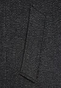 Teksturowana tkanina w kolorze węglowym z wzorem w jodełkę; posiada prostokątną kieszeń na łatkę. Materiał wygląda na wełniany i trwały.