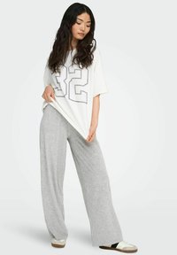 T-shirt bianco oversize con un grande numero nero "32" stampato sul davanti, abbinato a pantaloni ampi grigi chiari in tessuto morbido.