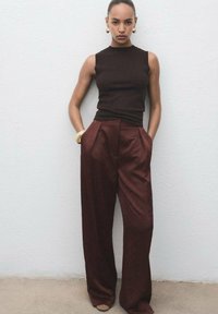 Top bej cu mânecă scurtă, asortat cu pantaloni lărgați, cu talie înaltă, de culoare vișinie. Prezintă texturi fine și un design minimalist.